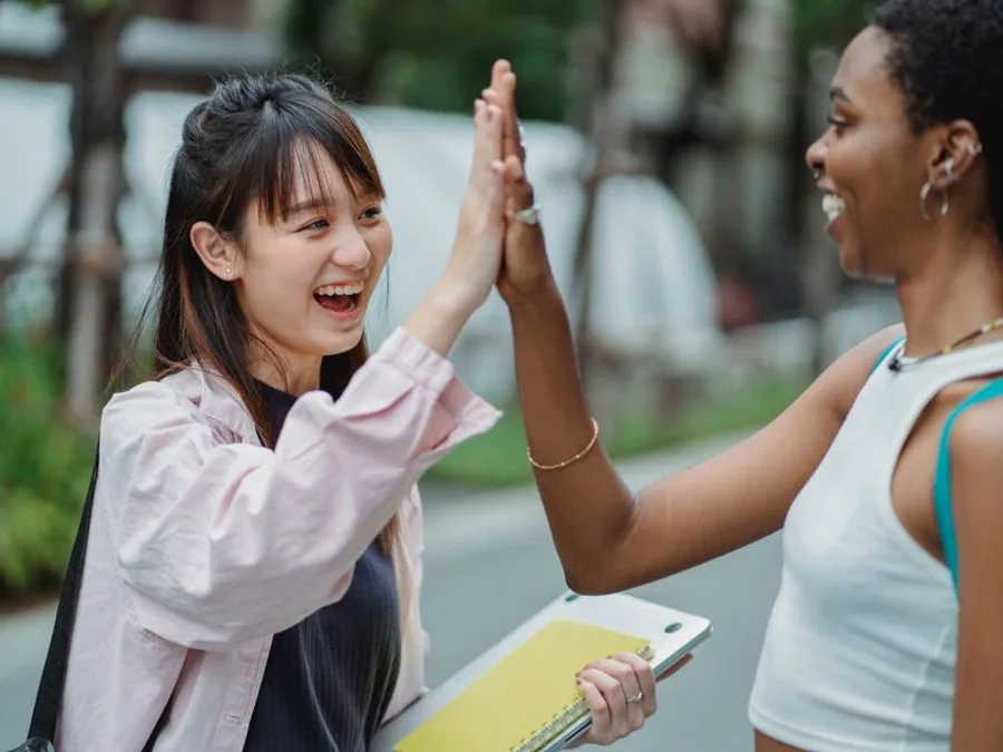 Two students from different backgrounds high-fiving on campus