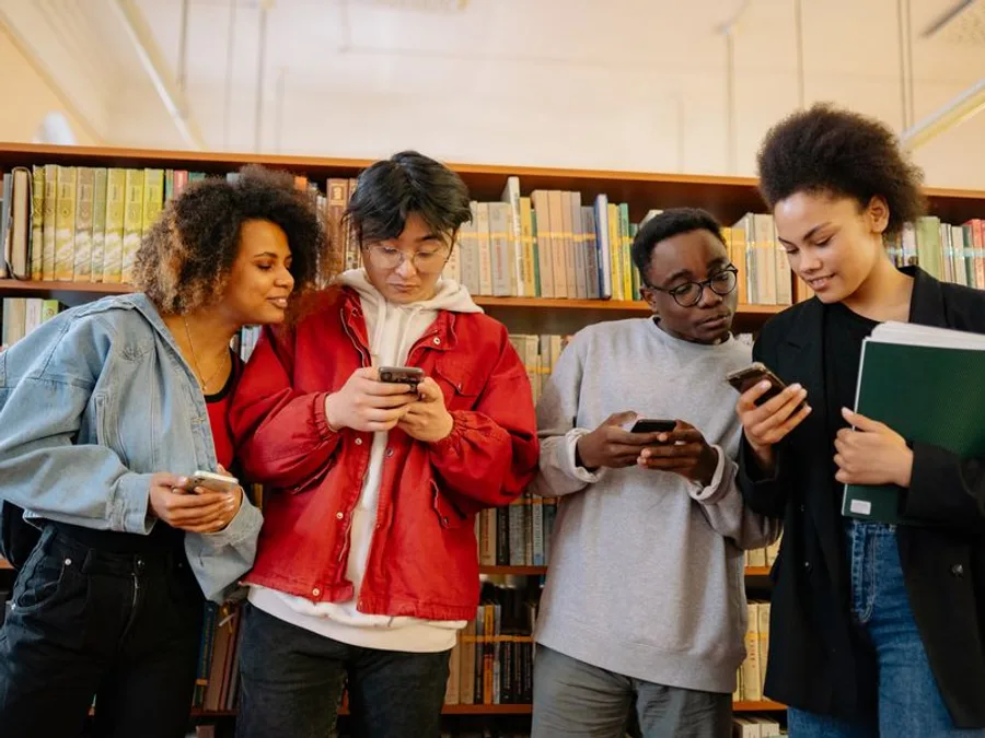 A diverse group of students checking their phones together in a library